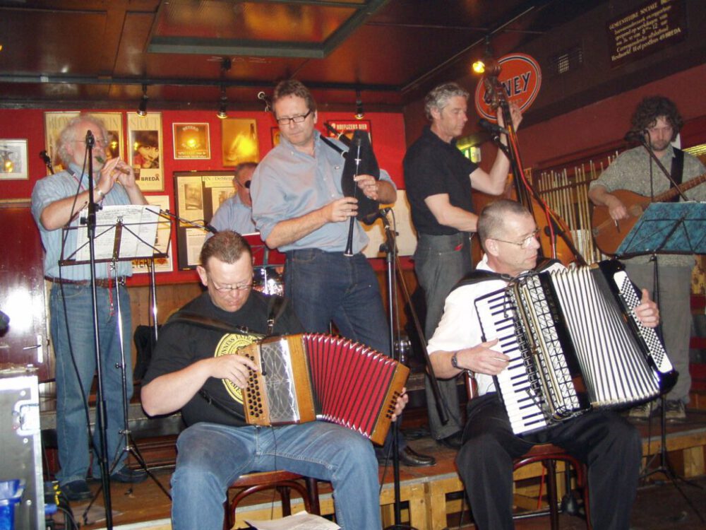 zes mannen die muziek maken met accordeons, doedelzak, fluit en snaarinstrumenten