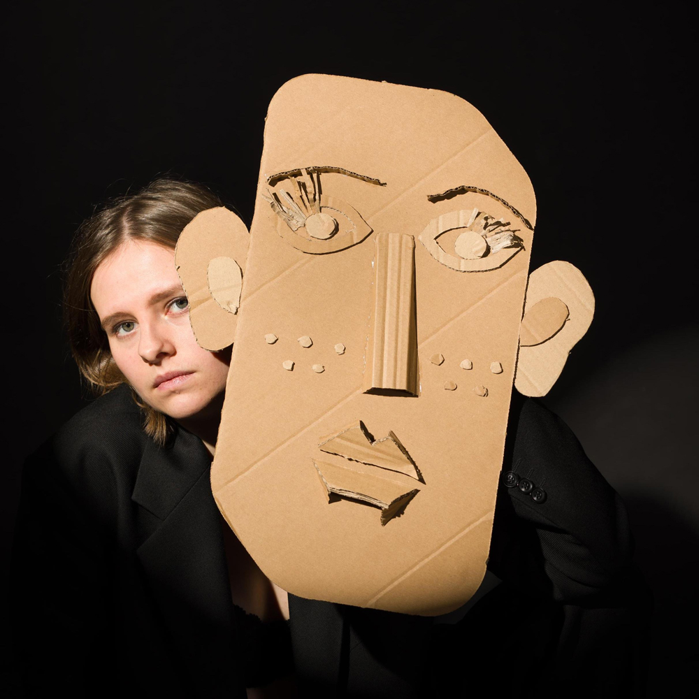 Renee Goris achter een groot papieren masker