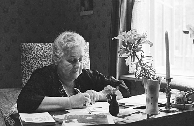 Anna Achmatova schrijvend aan een bureau met een bloem