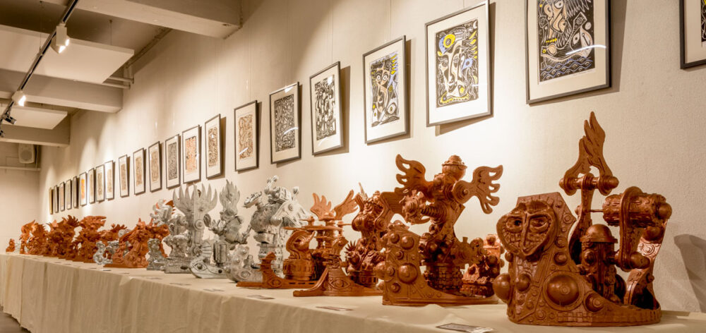 tafels langs de muur met bronskleurige sculturen en schilderijen aan de muur gezien van de zijkant.