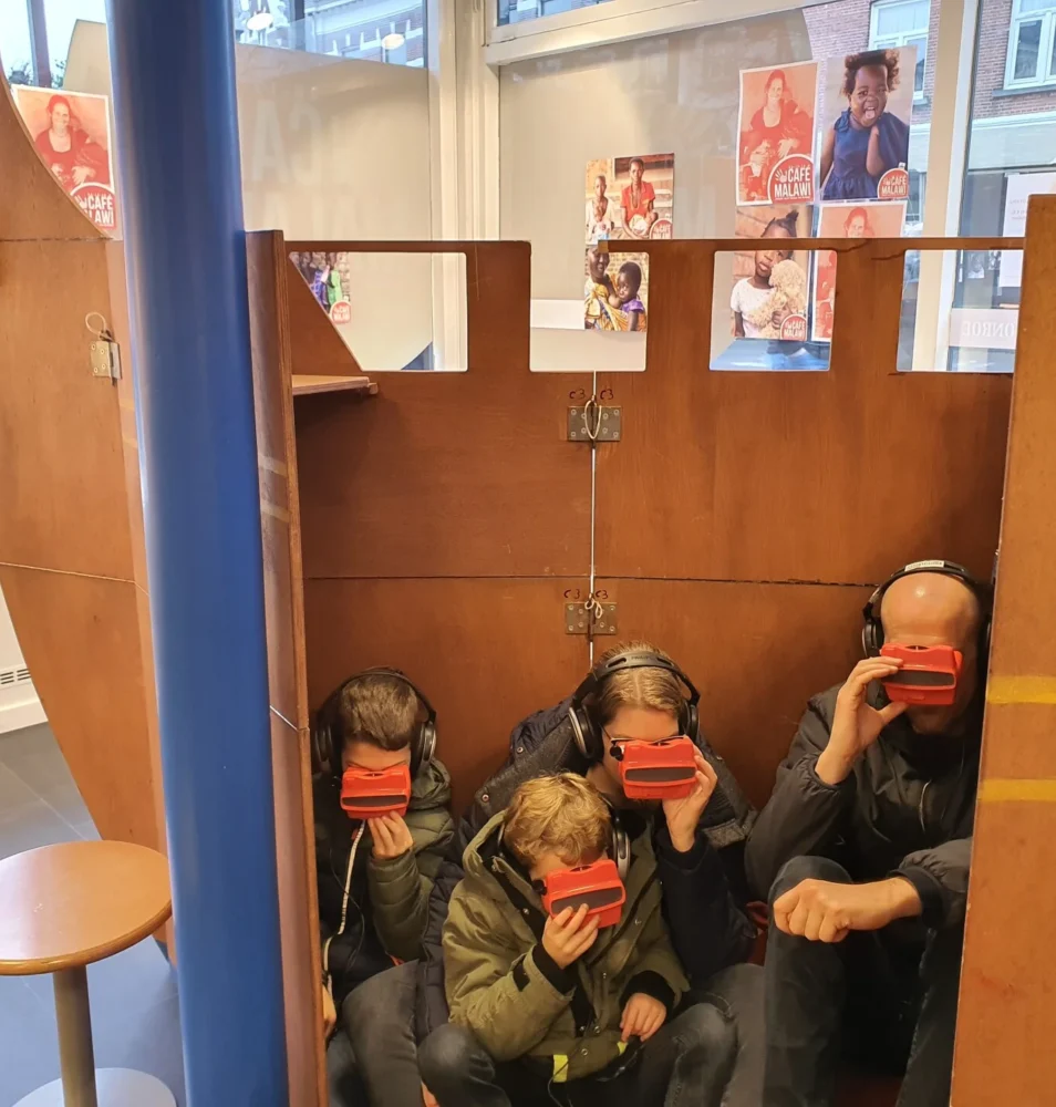 Twee kinderen en twee ouders ziitend in het argonautenschip met rode viewers waarmee ze illustraties van het verhaal bekijken