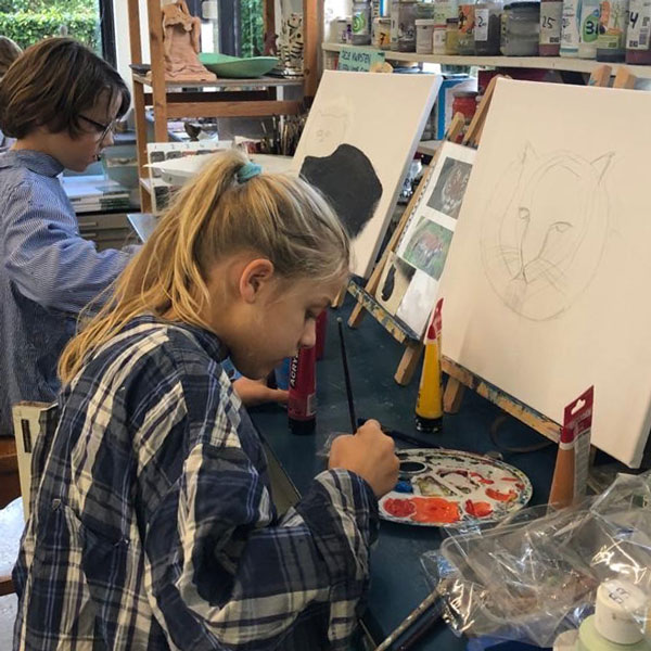 Meisje achter een schildersezel heeft een poes getekend op een canvas en gaat het met kleur inschilderen tijdens kinderkunstklas