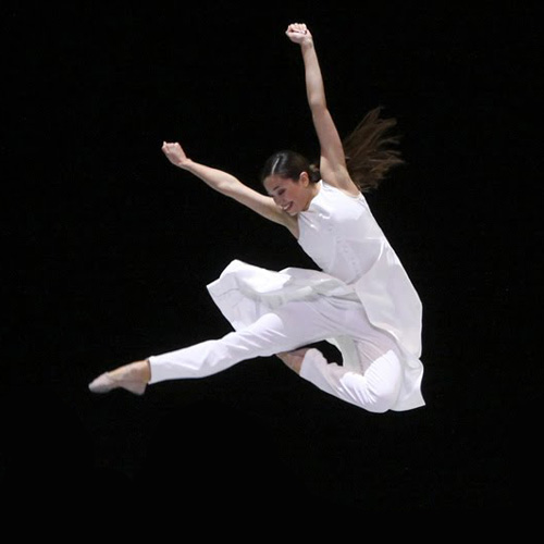 Springende balletdanseres in witte kleding tegen een donkere achtergrond