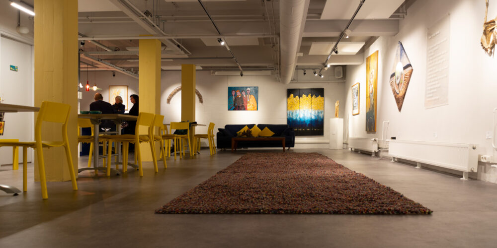 Een zitbank en meerdere schilderijen in de expositieruimte van Het Gele Huis tijdens de expositie Troost en Hoop