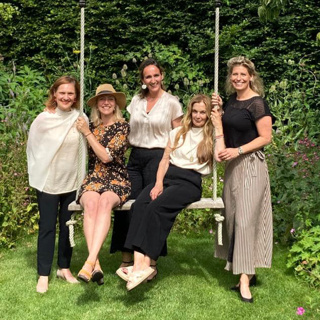 Vijf vrouwen op en bij een schommel in een groene tuin
