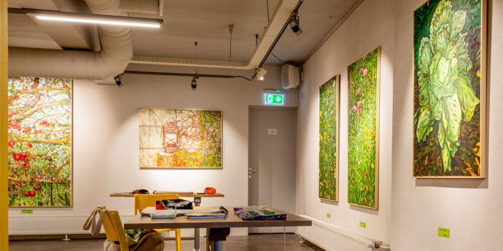 overzicht met diverse schilderijen van volkstuinen met veel groen en rood, in het expositieruimte van Het Gele Huis