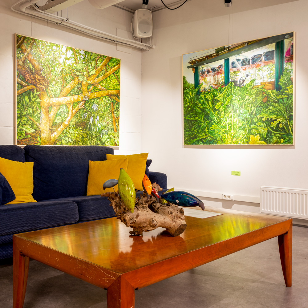 twee schilderijen van Paul der Kinderen met veel natuurgroen en een zitbank met kussens in de expositieruimte van Het Gele Huis
