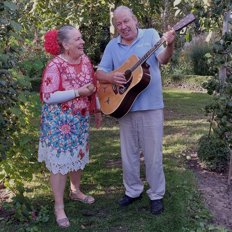 Conchita in Chileense klederdracht en Lorenzo met een gitaar staan in een groene tuin