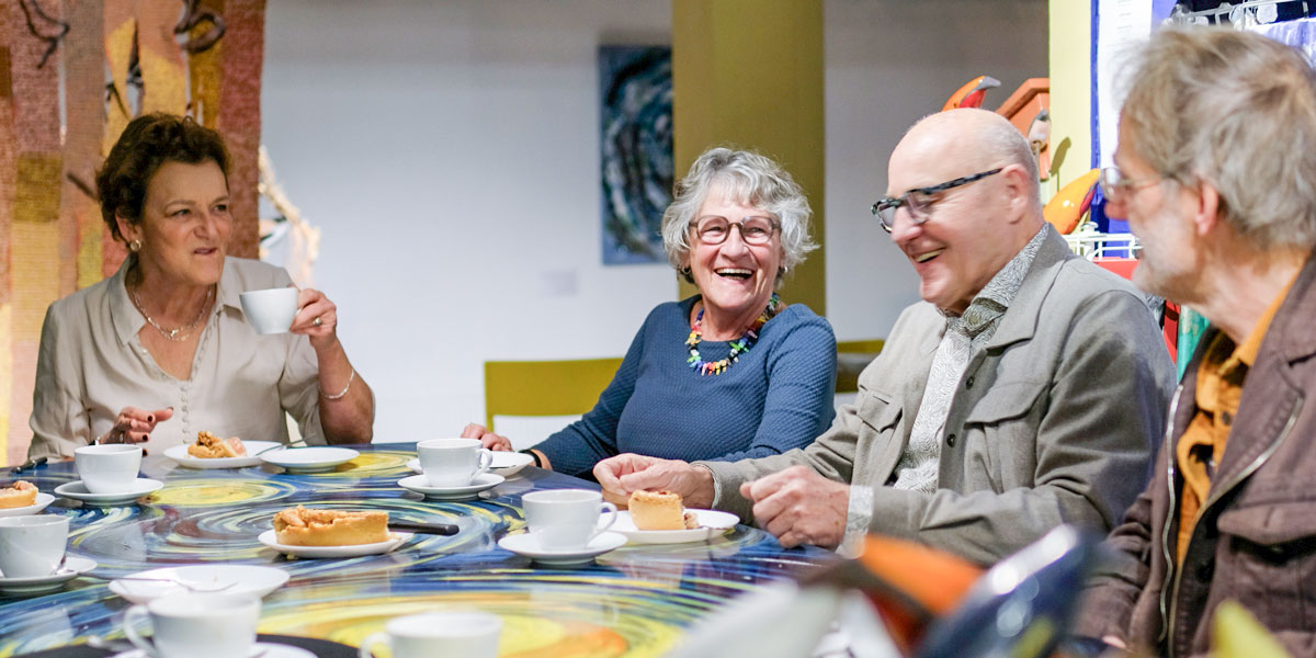 elkaar ontmoeten in Het Gele Huis: lachende personen aan een mooi geschilderde tafel