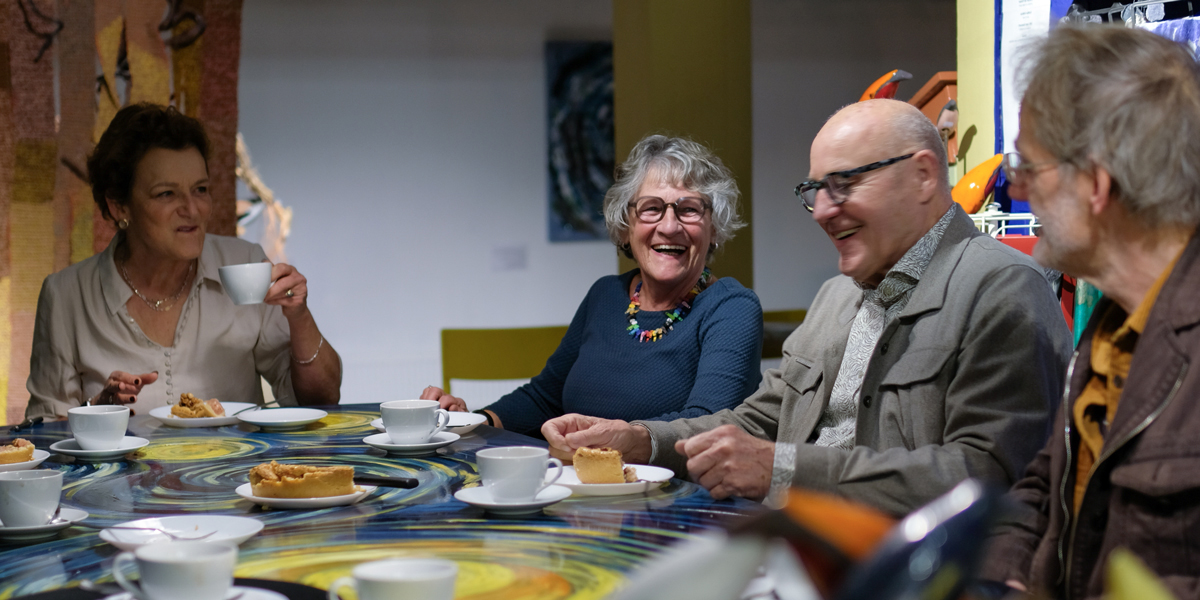 elkaar ontmoeten in Het Gele Huis: lachende personen aan een mooi geschilderde tafel